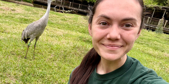 A selfie of Nichole Moore with a banded Sandhill Crane in the background.