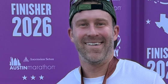 Chris Strojan posing in front of a banner for finishers of the 2026 Austin Marathon.