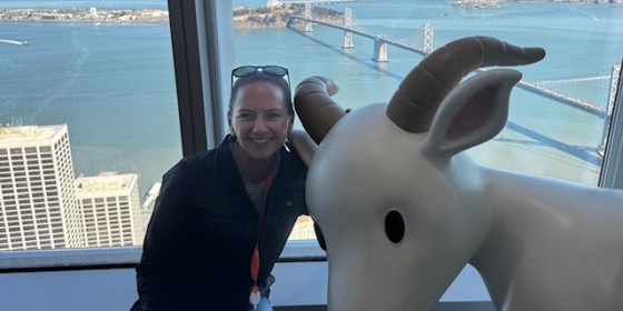 Stacie Johnson posing with a statue of a goat in front of a high window with lower buildings and a waterfront in the background.